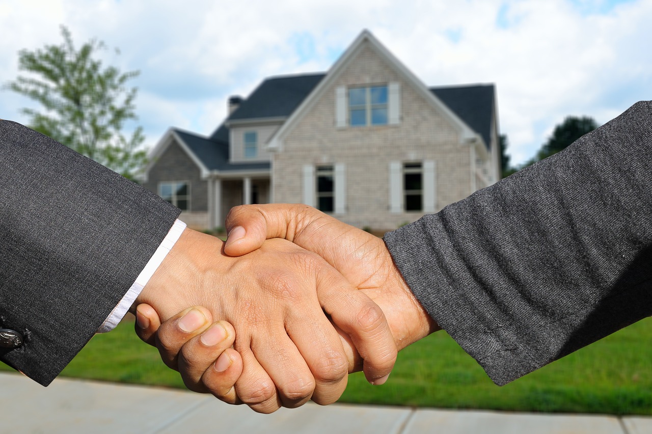 Immobilienmakler und Kundin geben sich vor einem Haus die Hand